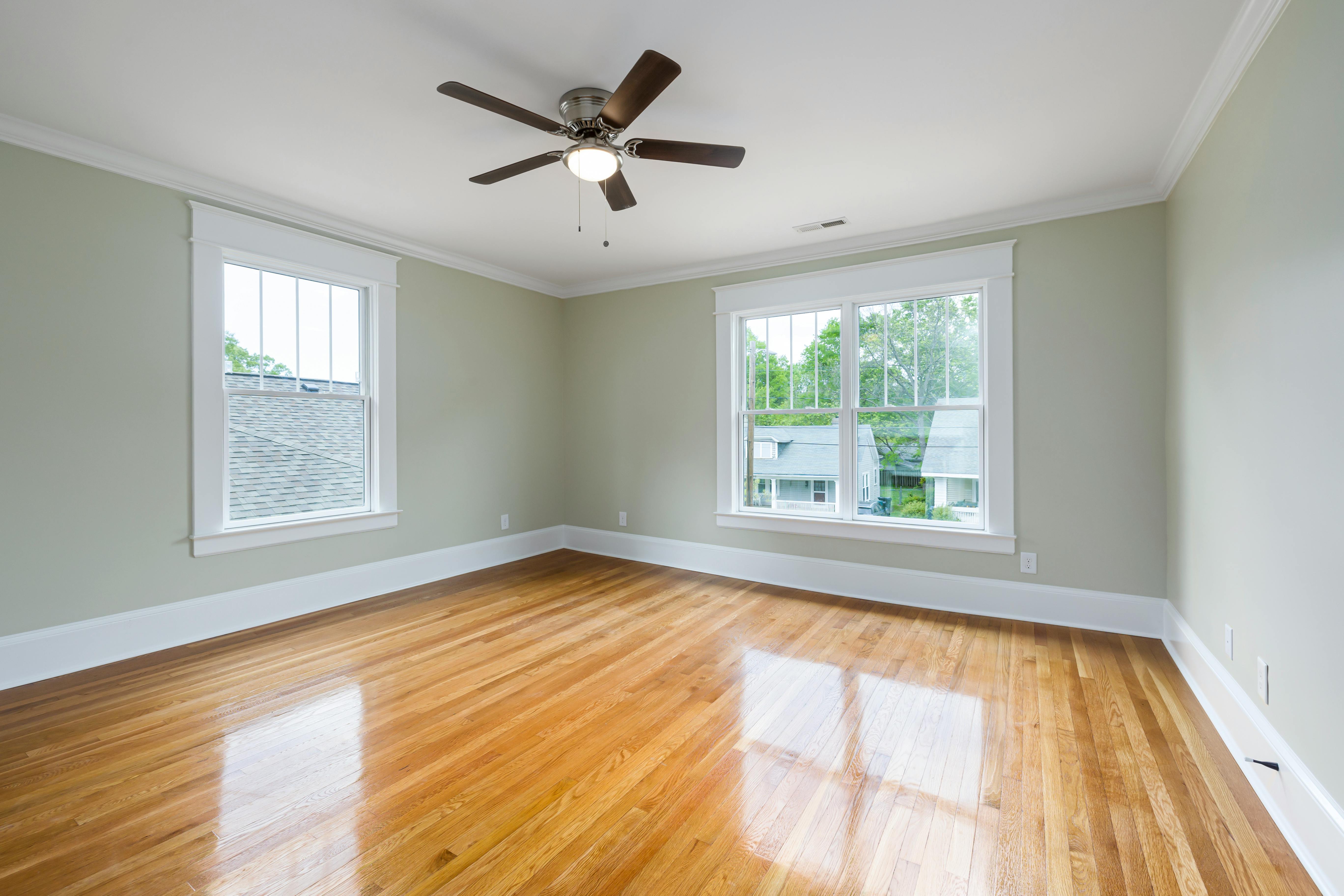 Service Bright empty room with wooden floors, large windows, and a ceiling fan.