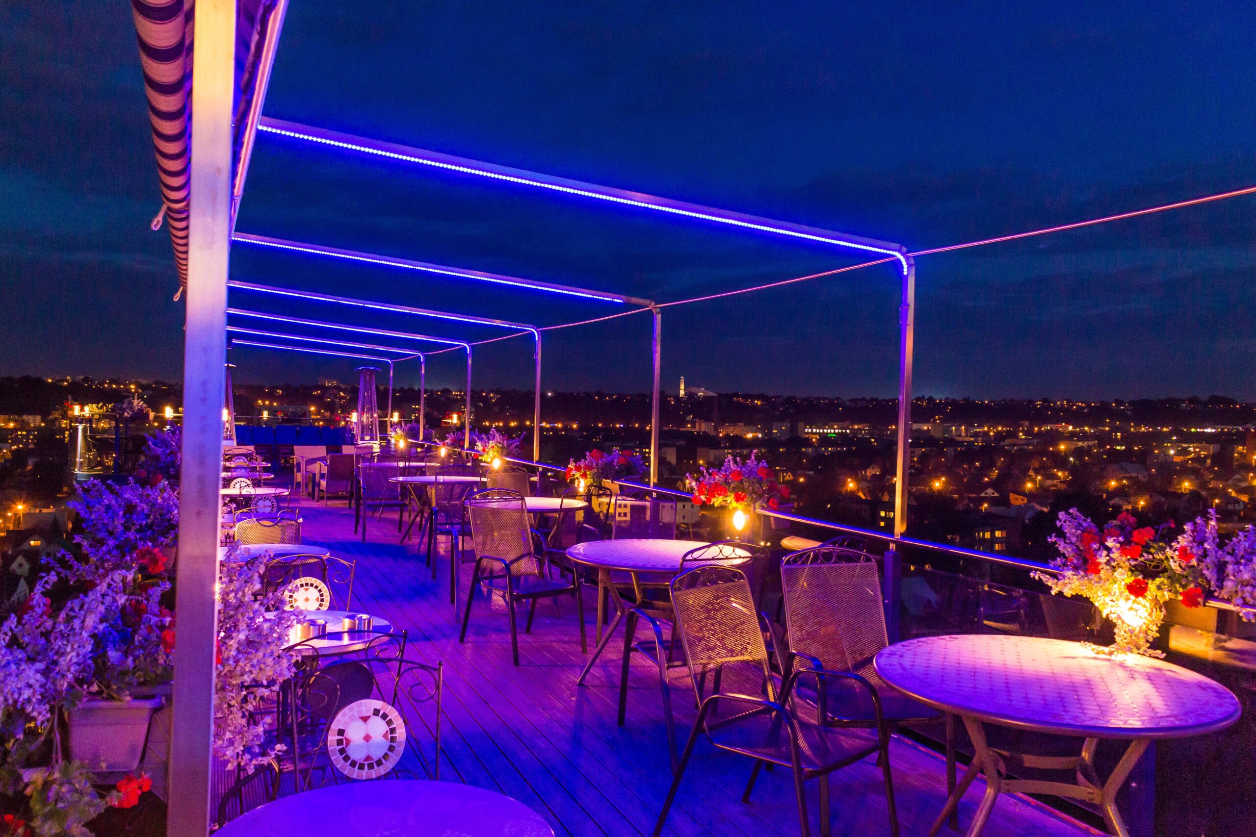 Vibrant rooftop terrace illuminated by neon lights with a stunning cityscape backdrop at night.