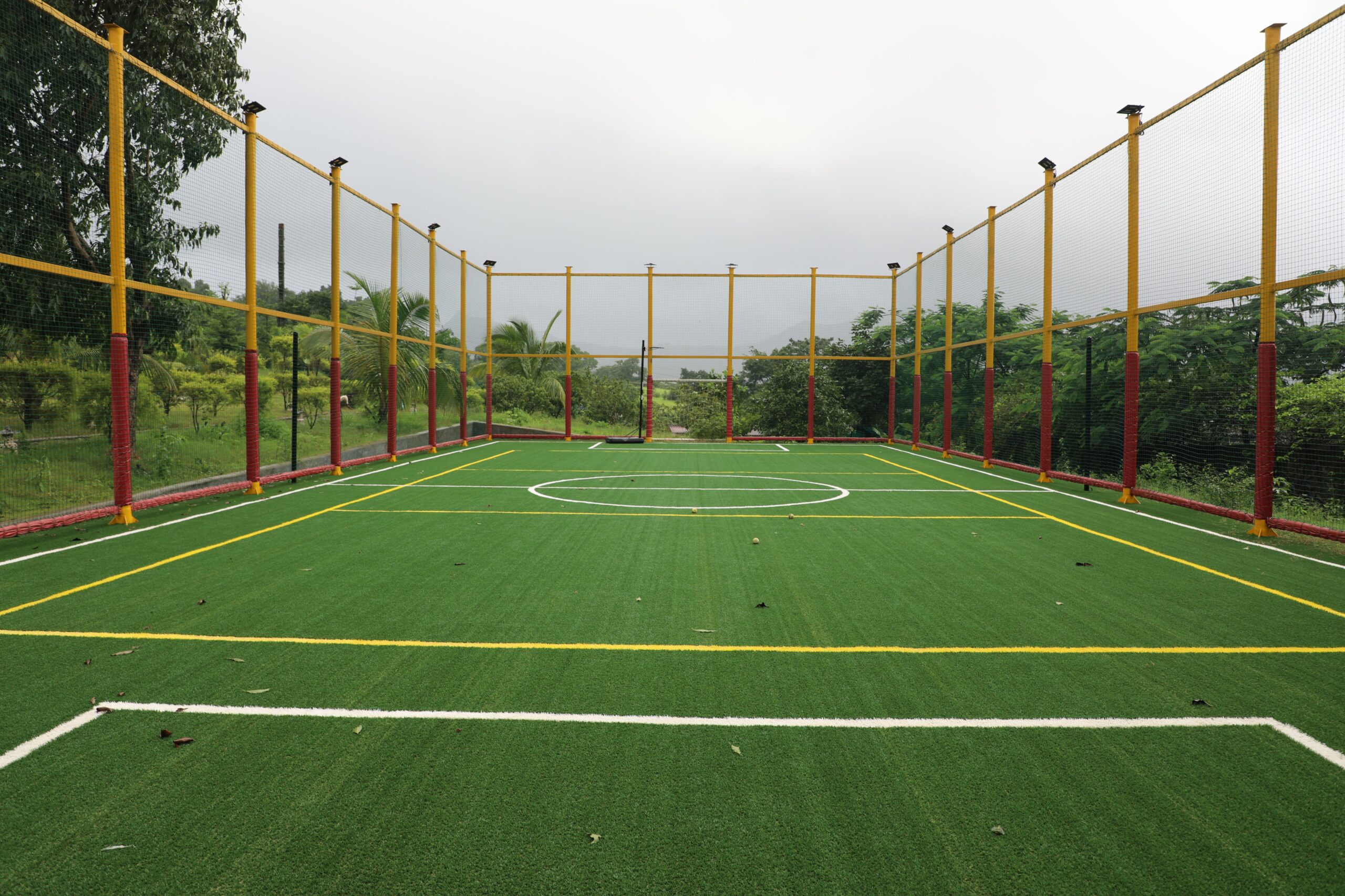 Service Vibrant outdoor futsal court with artificial turf surrounded by a net in a lush setting.